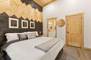 Cabin bedroom with a king bed, mountain-themed wood accent wall, and rustic decor. Perfect inspiration for those looking to build a custom cabin with our Kentucky cabin building company.