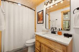 Bathroom in a newly constructed cabin, featuring a light wood vanity with a granite countertop, a white toilet, and a shower with a white curtain. "Red River Gorge" poster on the wall. Thinking of building a cabin? Contact us!