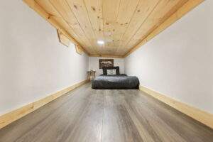 Cozy cabin bedroom nook featuring a low platform bed with gray bedding, a side table, and a rustic wooden ceiling. The room showcases efficient space utilization, highlighting potential for custom cabin construction.