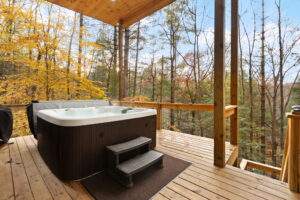 A luxurious hot tub sits on a wooden deck, steam rising into the crisp autumn air. Surrounded by colorful fall foliage, this cabin's outdoor space offers relaxation and connection with nature. Perfect for a custom-built Kentucky home.
