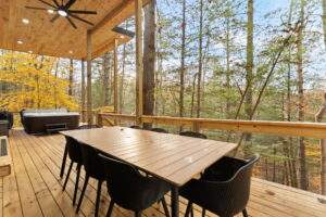 Covered porch with a dining table and hot tub overlooking a forest. Consider our cabin building company for custom-built homes and cabins in central and eastern Kentucky, including the Red River Gorge.