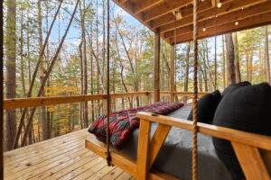 A cozy, custom-built cabin porch with a swinging bed, inviting relaxation amidst the Red River Gorge trees. This cabin, built by our construction company, blends seamlessly with the Kentucky landscape. Build your dream cabin with us!