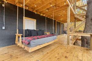Cozy porch swing on a wooden deck, part of a custom cabin built in Kentucky. Black cinder block wall and string lights add to the rustic charm. Build your dream cabin with us!