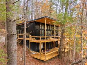 Black cabin with large windows in autumn forest, showcasing construction by Red River Gorge cabin builders in Kentucky.