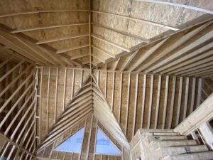 Interior view of a cabin under construction in the Red River Gorge, Kentucky, showing the intricate wooden framing of the walls, roof, and a triangular window. Highlights the craftsmanship involved in building a custom cabin.