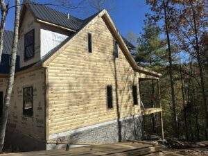 Cabin under construction, displaying raw wood siding and a metal roof. Tyvek HomeWrap is visible on an unfinished section, highlighting the building process. This custom-built home reflects quality construction.