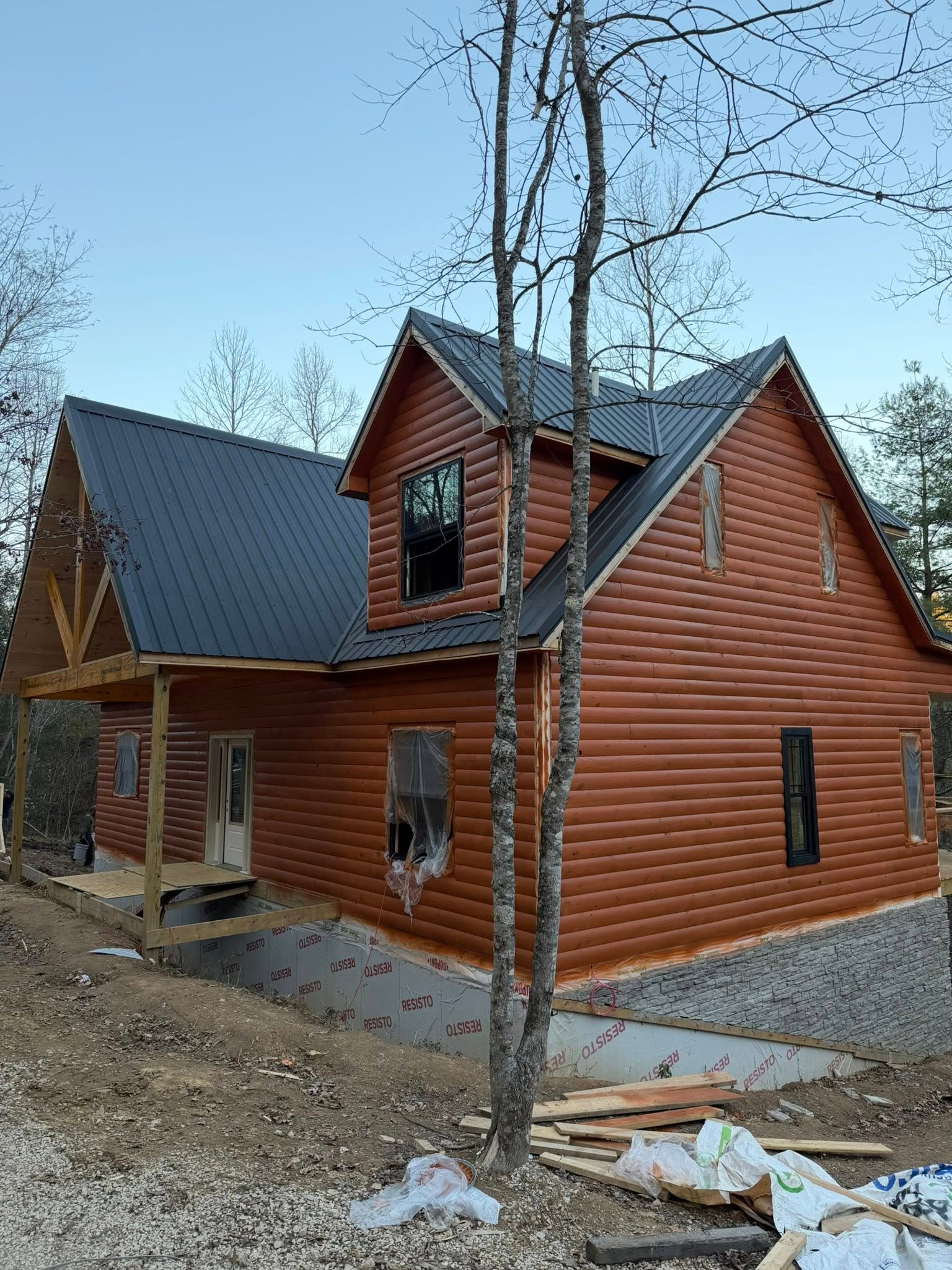 Cabin under construction in the Red River Gorge, Kentucky. A rustic, brown-sided cabin with a dark metal roof and exposed timber framing on the porch, showcasing a beautiful short-term rental investment opportunity.