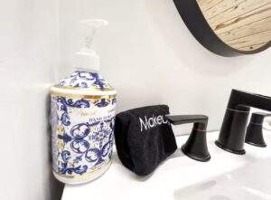 Bathroom sink with a bottle of decorative "Pretend Hand Soap", a black makeup towel, and a modern black faucet. The photo highlights the details of a bathroom in a custom-built home.