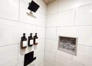 Modern shower with white subway tile, black fixtures, and a built-in shelf with mosaic tile. This cabin's bathroom shows the quality of our construction. Build your dream cabin with us!