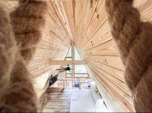A-frame cabin interior with exposed wood beams and a view of the living area below. Natural light floods the space, highlighting the craftsmanship of our custom cabin construction in Kentucky. Build your dream cabin with us!
