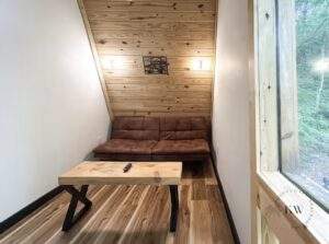 Cozy cabin nook featuring a brown futon under a wood-paneled ceiling with sconces. A rustic wood coffee table sits on wood floors, showcasing the craftsmanship of our cabin building company in the Red River Gorge.