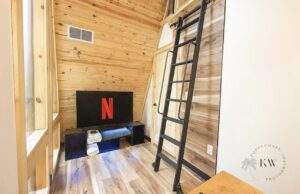 Cozy cabin interior in Red River Gorge, Kentucky. Wood paneling, ladder to loft, and TV with Netflix logo. Perfect for relaxing in your custom-built cabin. Contact our cabin building company today!