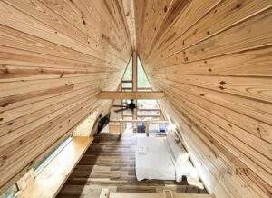 A-frame cabin interior in Red River Gorge, KY, showcasing wood-paneled walls, ceiling fan, and a cozy bed. This cabin, built by our construction company, exemplifies the charm of cabin living in the Red River Gorge.