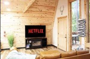 Cozy cabin interior featuring a TV screen displaying "NETFLIX", nestled in a wooden A-frame structure. Relaxing getaway with a rustic touch, perfect for a custom built home in the Red River Gorge.