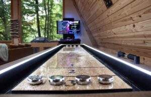 A custom-built shuffleboard table inside a Red River Gorge cabin, showcasing craftsmanship by our cabin building company. The game table sits beneath a TV, with a lush forest view visible through a large window.