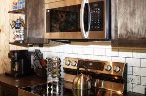 Cozy cabin kitchen featuring a stainless steel microwave over a glass cooktop, dark wood countertops, and custom wood cabinets. Perfect example of our cabin building company's craftsmanship in the Red River Gorge.