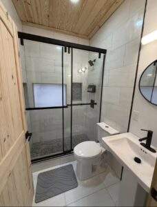 Modern cabin bathroom with wood ceiling, white tile walls, and black framed glass shower. Built by our cabin building company, showcasing quality construction in the Red River Gorge area.