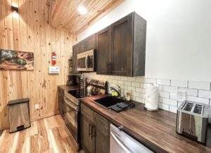 Cabin kitchen featuring dark wood cabinets, stainless steel appliances, and a light wood plank wall. A modern design showcasing quality construction, ideal for a custom-built home in Kentucky from our cabin building company.
