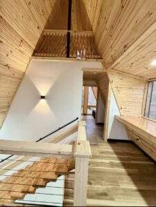 Interior view of a modern cabin in Red River Gorge, Kentucky. Features include wood-paneled walls, a staircase with cable railings, and a hallway leading to a bright room. A custom-built home showcasing cabin construction.
