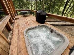Hot tub on a wooden deck surrounded by trees. Cabin building in the Red River Gorge offers outdoor living with custom-built homes, perfect for relaxation and enjoying nature in central Kentucky.