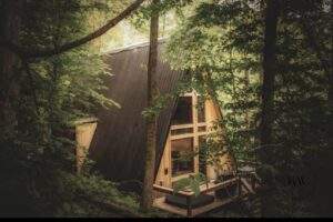 A-frame cabin nestled in a lush, green forest in Red River Gorge, Kentucky. Modern construction with large windows showcases the beauty of custom-built homes by our cabin building company.