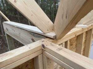 Cabin construction detail: wooden beams forming a roof truss on a partially built structure, showcasing craftsmanship. Ideal for those considering cabin building in Kentucky.
