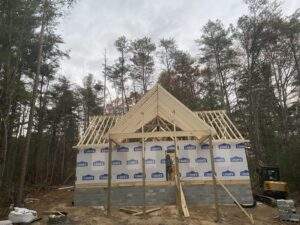 New cabin construction in Kentucky, featuring a framed structure with Lowe's house wrap, set against a backdrop of tall trees. Part of our custom-built homes and cabin building company projects.