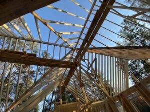 Cabin construction in Red River Gorge, Kentucky. Wooden beams form the skeleton of a custom built home under a blue sky, showcasing the detailed framework of our cabin building company.