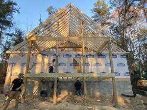 Cabin construction in Red River Gorge, Kentucky. Workers frame the gable roof on a partially built cabin, showcasing the building process with lumber from Lowe's. Foundation is cinder block.