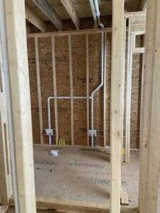 Incomplete plumbing for a new cabin build by our Kentucky construction company. Pipes and electrical boxes are visible inside the framed wall, showcasing the early stages of a custom home build.