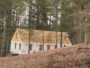 Cabin construction in progress nestled in a wooded lot in Kentucky. Framing is up, wrapped in Tyvek HomeWrap, showing the early stages of a custom-built home by our cabin building company.