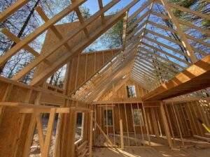 Cabin construction in progress: exposed wood framing and rafters against a blue sky. Build your dream cabin in the Red River Gorge with our custom building company.