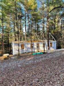 Cabin construction in a wooded area. The framed cabin is wrapped in Tyvek HomeWrap, highlighting the building process. Build your custom cabin with our Kentucky cabin building company.