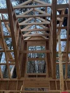 Cabin construction in Red River Gorge, Kentucky. A framed view of a partially built cabin reveals the intricate wooden framework against a backdrop of trees, highlighting the craftsmanship of our cabin building company.
