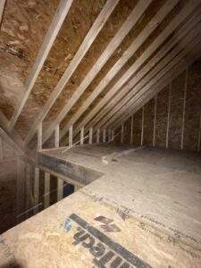 Unfinished attic space shows exposed rafters and OSB subflooring, highlighting construction details. Consider building with our custom cabin building company in Kentucky.