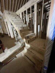 Partially constructed wooden staircase in a home under construction, showcasing the framing and initial steps. A ladder provides access to the upper levels, emphasizing the building process. Consider building with our Kentucky cabin building company for custom homes.