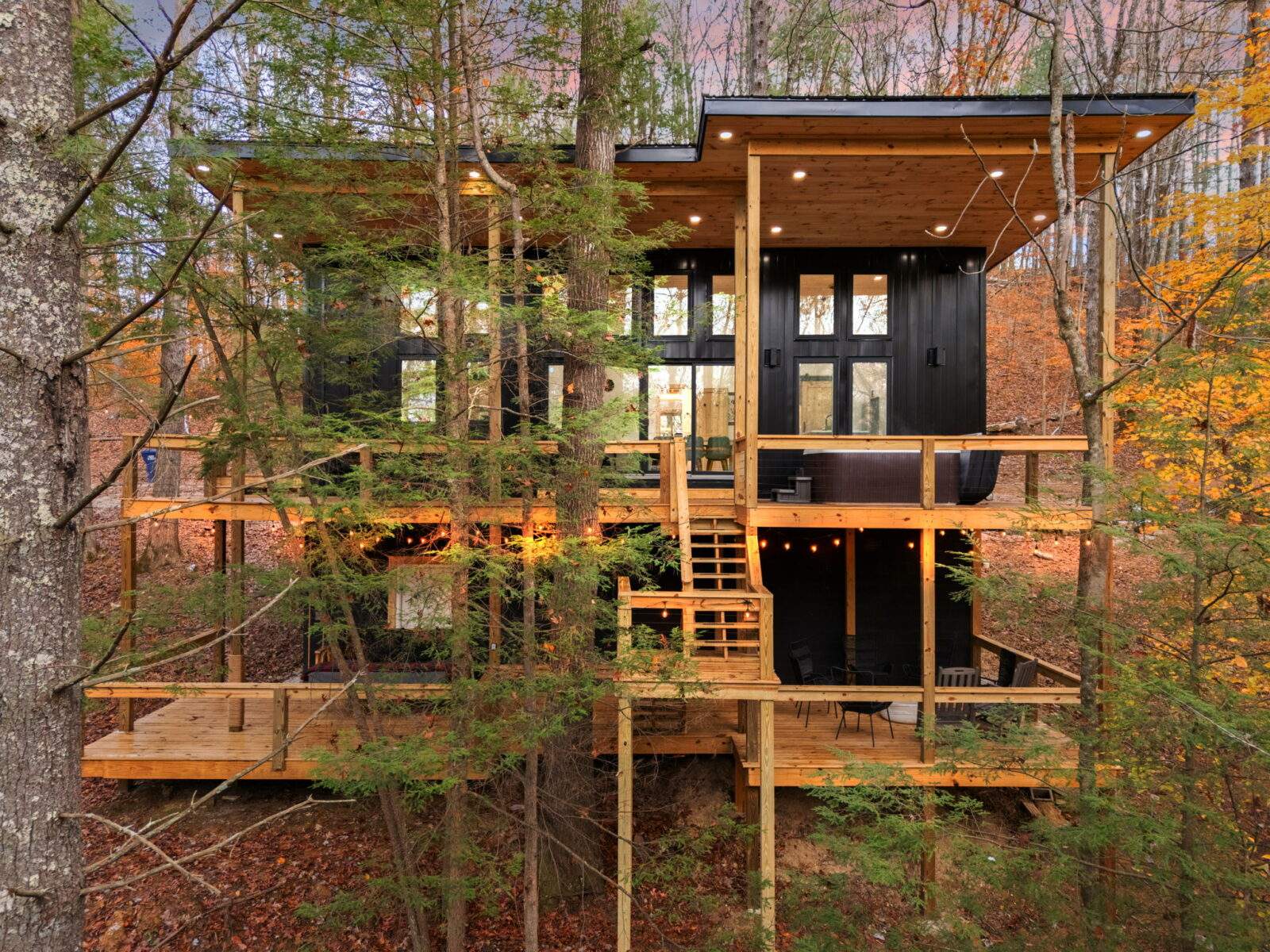 Modern cabin nestled among trees in Red River Gorge, KY. This multi-level structure features black siding, wood decks, and large windows, blending seamlessly with the natural Kentucky landscape. Consider building a cabin with us!